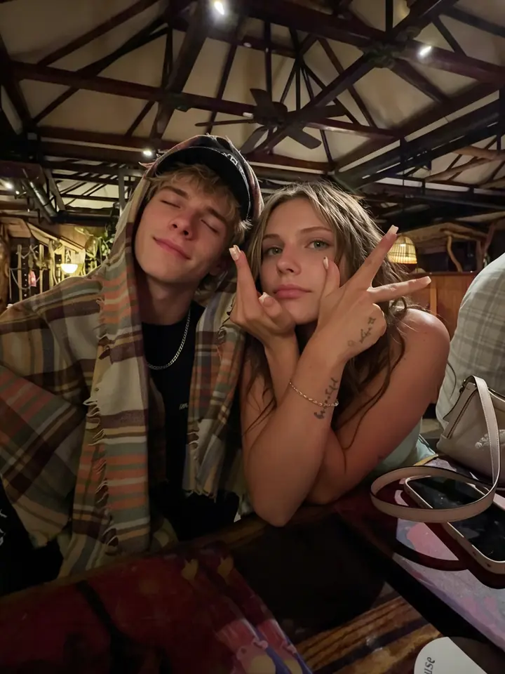 Una pareja joven posa haciendo el signo de la paz en un bar bajo un techo de madera