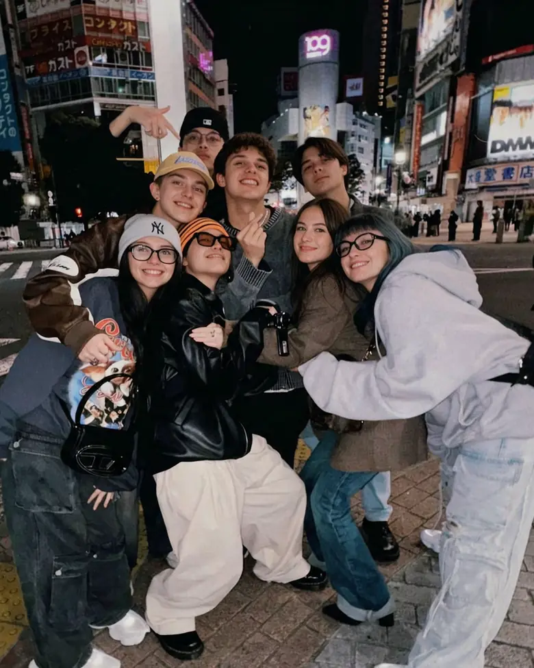 Un gran grupo de amigos abrazándose y posando en una esquina de Shibuya, Tokio, de noche